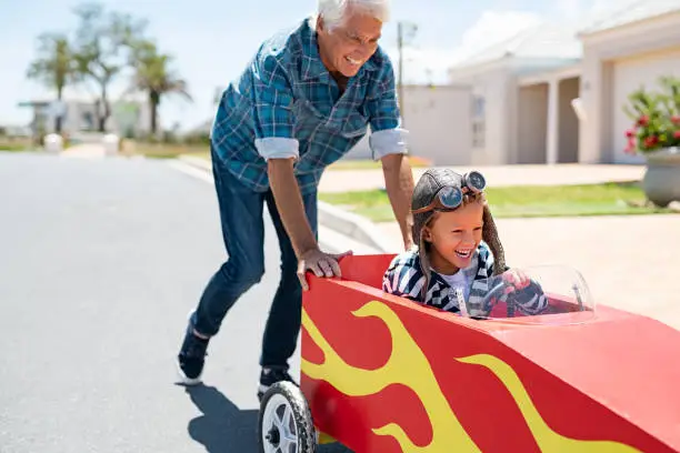 Photo of Grandfather pushing his little boy on toy car