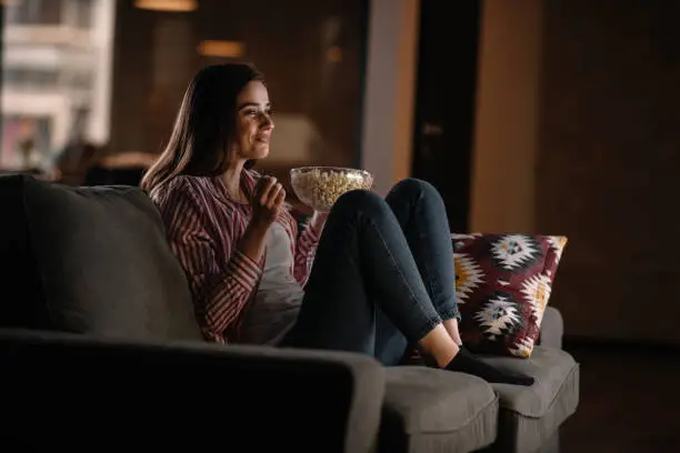 Photo of Beautiful woman watching movie in the night sitting on a couch in the living room at home