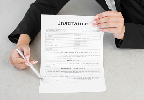 A young woman in suit in office showing an insurance policy and pointing with a pen where the policyholder must to sign