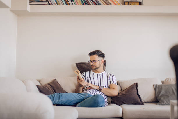 istock Happy young man reading a book and enjoying on the sofa 1256108998