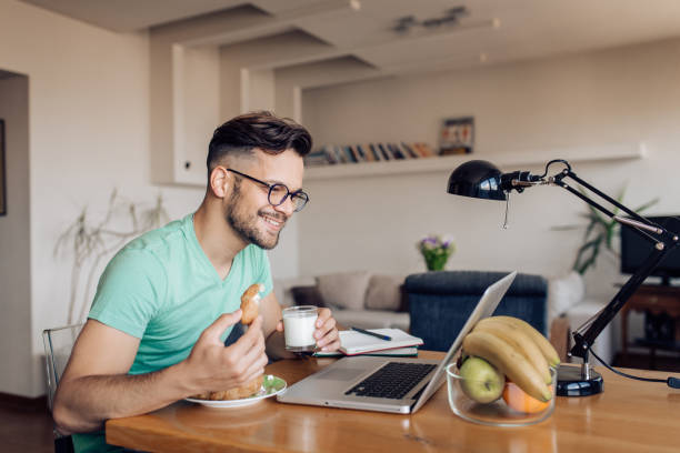 istock Young man eating a croissant and working from home 1256109597