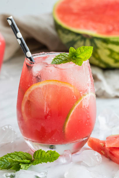 A watermelon drink watermelon, lemon, lime, mint and ice Watermelon mojito fresh red drink. With watermelon, lemon, lime, mint leaves and ice. The drink is on a white table with a half watermelon in the background and ice and mint scattered on the table. frozen rose stock pictures, royalty-free photos & images