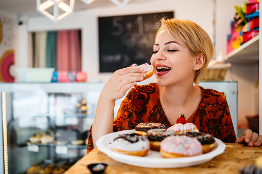 Young blond woman enjoying eating great donut at the bakery store.