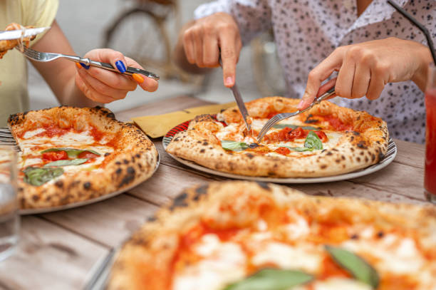 Close up of male's and female's hands cutting a freshly baked pizza Margherita on the table.