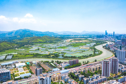 Drone view of rural green fields with fish ponds on Hong Kong and the skylines of Shenzhen