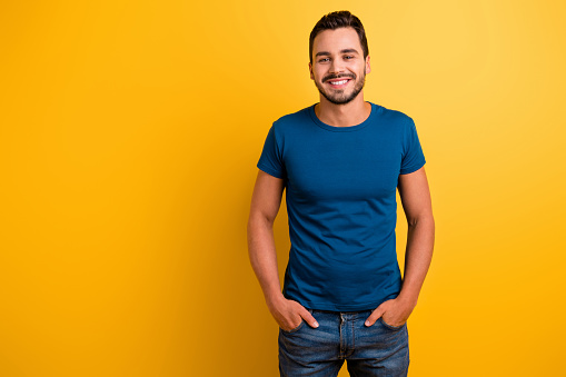 Portrait of his he nice attractive glad cheerful cheery brunette guy holding hands in pockets, isolated over bright vivid shine vibrant yellow color background