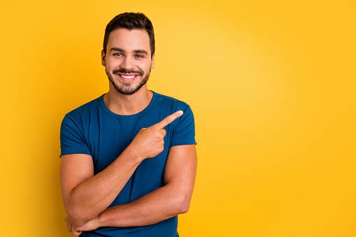 Close-up portrait of his he nice attractive glad cheerful cheery guy pointing forefinger aside recommend presentation isolated over bright vivid shine vibrant yellow color background