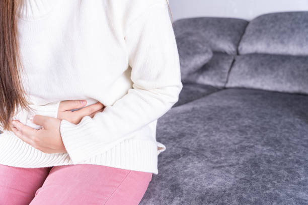 istock Young woman suffering from strong abdominal pain or menstruation while sitting on sofa at home. Healthcare medical or daily life concept. 1256129437