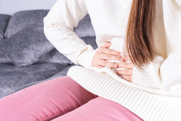 istock Young woman suffering from strong abdominal pain or menstruation while sitting on sofa at home. Healthcare medical or daily life concept. 1256129471