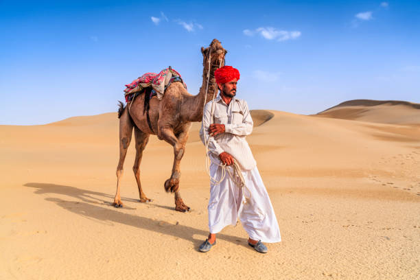 istock Indian man holding camel on sand dunes, Rajasthan, India 1256129709