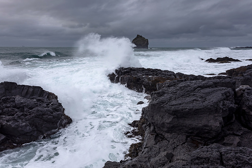 The harsh Icelandic coast with big waves beating against black rocks on a cloudy evening in the West of Iceland