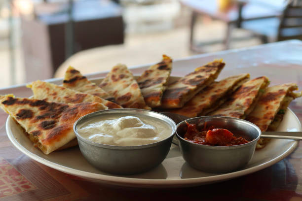 immagine ravvicinata del buffet del piatto della colazione indiana, fette triangolari di aloo paratha con cospargere di cipolla caramellata, su piatto bianco, pane salato ripieno di patate garam masala, piatto aloo paratha ristorante dell'hotel, yogurt cag - triangle human hand house home interior foto e immagini stock