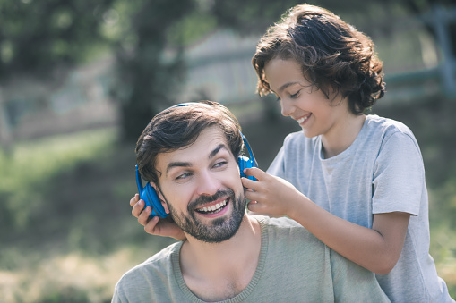 Earphones. Smiling son putting earphones on his fathers head