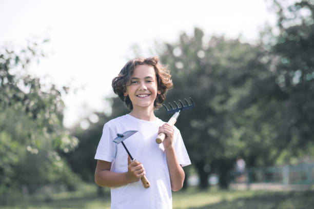 istock Dark-haired boy holding gardening equipment and smiling 1256137897