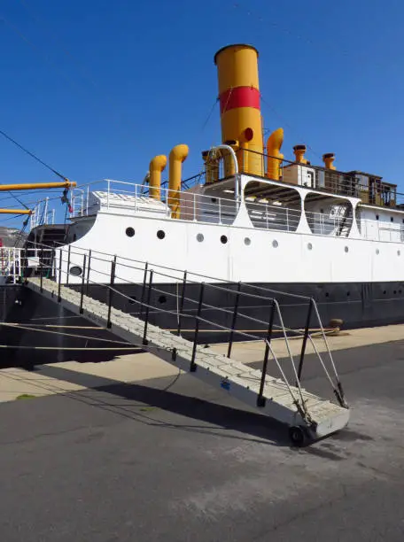 Close-up of merchant ship gangway with original yellow and red funnel or chimney under deep blue sky. Side view of deck and chimney of ferry.