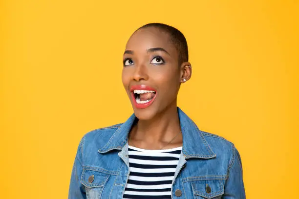 Close up portrait of happy young African American woman rolling her eyes looking up with mouth open in isolated studio yellow background