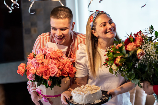 28-year-old Latin woman has her birthday cake in her hand while next to her is her 25-year-old Latin man friend who carries her the roses he is giving her for her birthday