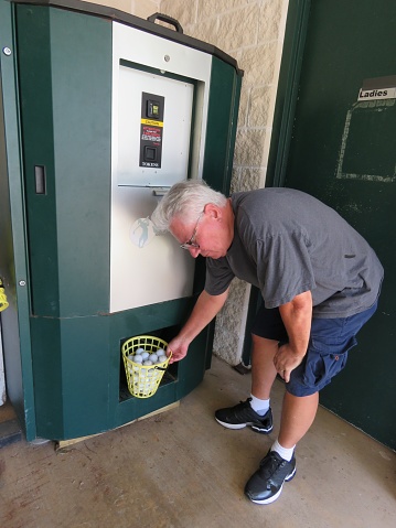 Senior Man gets golf balls from dispenser machine to practice golfing at driving range.