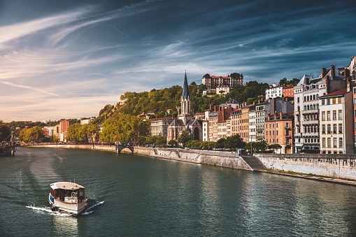 Saone riverbank in Lyon old town, Vieux Lyon district, with the Saint-Georges church majestic monument, a tourist tourboat sailing and colorful residential apartments. Taken in Lyon city, Unesco World Heritage Site, in Rhone department, Auvergne-Rhone-Alpes region in France during a sunny summer day.