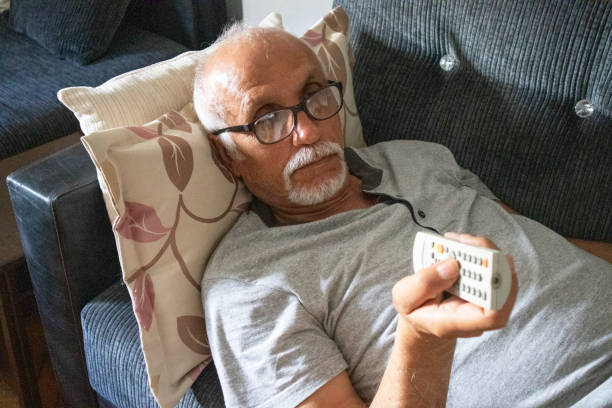homme aîné s’étendant sur le sofa et regardant la tv - television boredom men sofa photos et images de collection