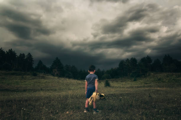 Abandoned sad child with a plush toy in his hand looking for mom. Sad story. Upset baby. Single orphan child on a background of dark forest. Neglected child. Sad baby. lost stock pictures, royalty-free photos & images