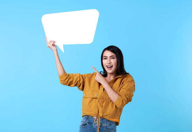 istock Smiling happy asian woman holding blank speech bubble and with empty space for text on blue background. 1256153365