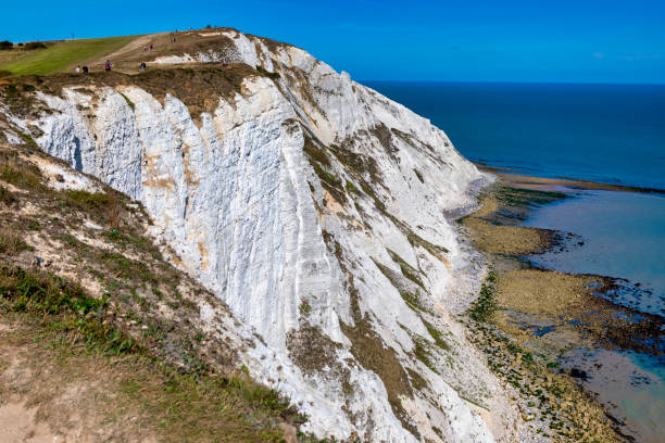 White cliff juts out over the sea below.  Silhouettes of people