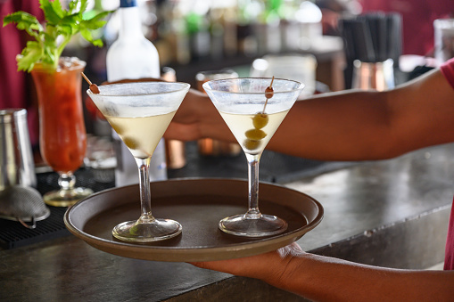 Close-up of unrecognizable waitress in sidewalk cafe putting dry martinis on serving tray, blurred bar counter is in background, Nikon Z7