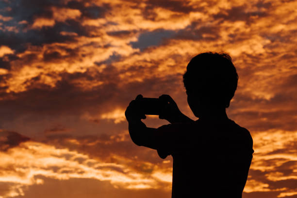 istock Silhouette of a kid using mobile phone in front of the sky during sunset 1256158065