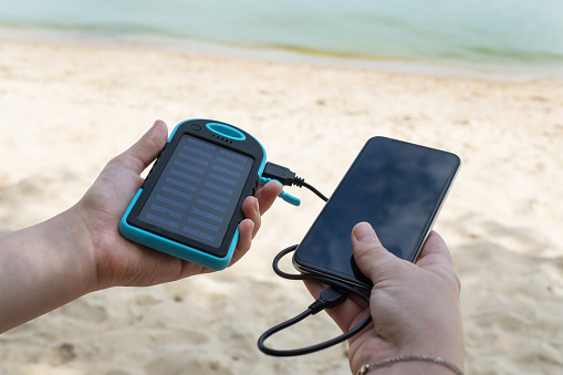 female hands hold solar powerbank in one hand and black smartphone in other. Trying to charge phone battery outside without electricity. Ability to stay in tough in any situation.