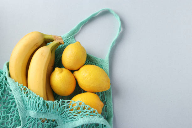 istock Yellow ripe bananas and lemons in turquoise string mesh bag on light background, Zero waste concept, Space for text 1256168562