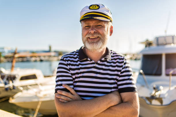 Mature man stands on pier dressed in a sailor's shirt and hat.