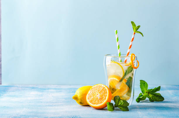 Refreshing cocktails with mint with lemon, orange, mint and ice Summer refreshing cocktails, lemonade or mojito with lemon, orange and mint with ice in a glass cup and with a striped paper straw. On a light blue background. Copy space. infused water stock pictures, royalty-free photos & images