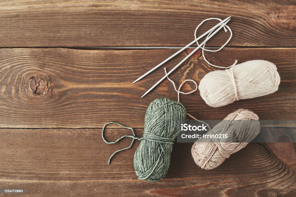 Balls of yarn on a wooden table Woolen threads of natural colors and knitting needles on a wooden background. Top view. Knitting Needle Stock Photo
