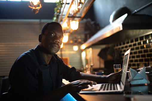 Portrait of a senior man working in a restaurant, using laptot