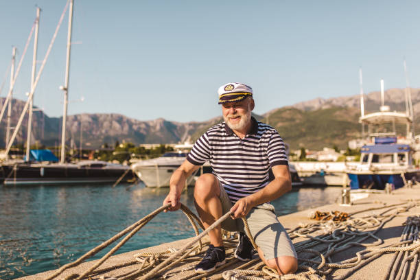 Mature man on pier dressed in a sailor's shirt and hat holding a sailor rope