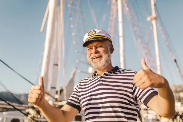 Mature man stands on pier dressed in a sailor's shirt and hat.