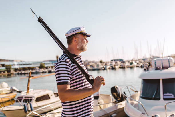 Mature man stands on pier holding a harpoon Mature man stands on pier dressed in a sailor's shirt and hat holding a harpoon harpoon stock pictures, royalty-free photos & images