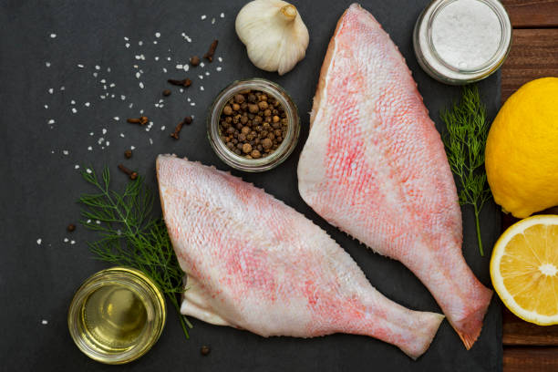 mariscos. posa en una pizarra negra. lubina roja sobre una tabla negra con los ingredientes para cocinar. pescado en la mesa. perca oceánica. - rockfish fotografías e imágenes de stock