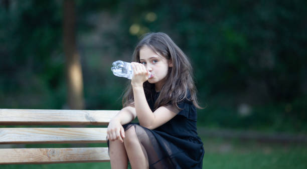 porträt eines kleinen mädchens 8 jahre alt mit langen haaren mit einer flasche wasser - children only photography drink 8 9 years stock-fotos und bilder