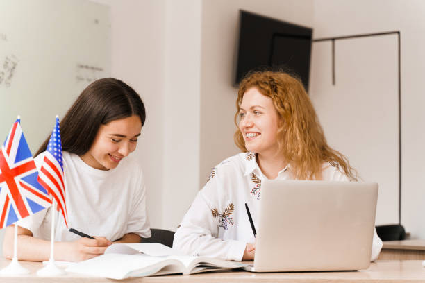 istock Foreign school private study with a school girl. Teacher explain grammar of native language using laptop. Prepearing to exam with tutor. English and British flags in front. 1256178560