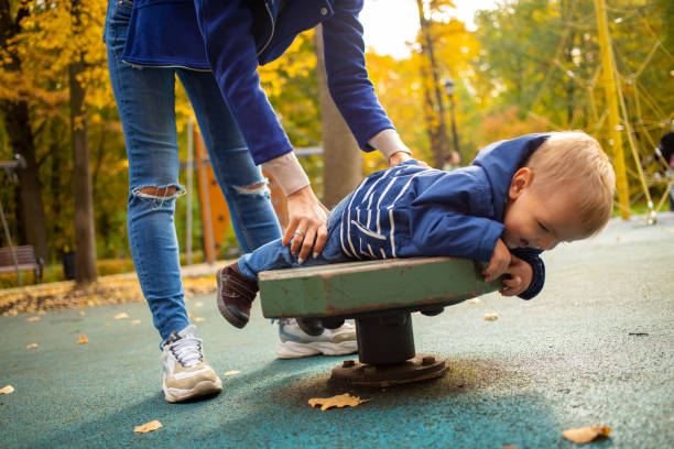 Mom and toddler in blue clothes play fun on the playground in the autumn park. happy childhood concept stock photo