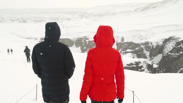 Back view of young couple walking in winter mountain together. Snowy mountain in Iceland