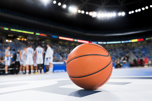 Empty professional basketball stadium illuminated with spotlights and tribunes full of fans who waiting favorite team made in 3D. Concept of sports betting, motion, action, team games in 2024.