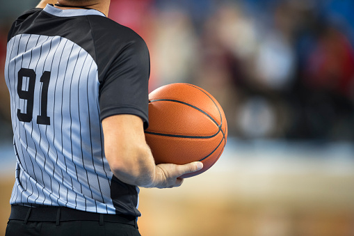 Mid section of referee holding basketball.