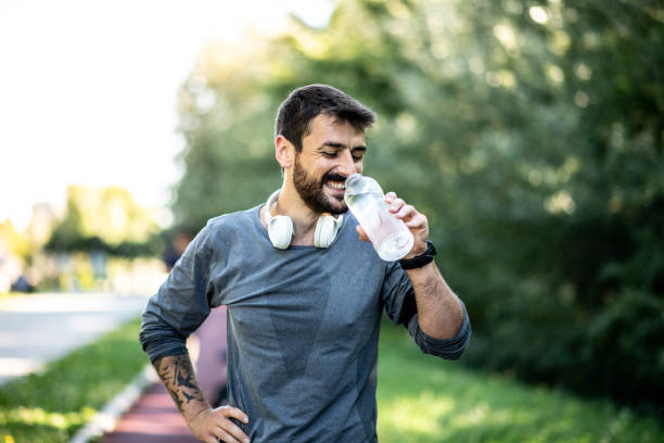 un giovane maschio caucasico magro è appoggiato su un tapis roulant e acqua potabile - drinking men water bottle foto e immagini stock