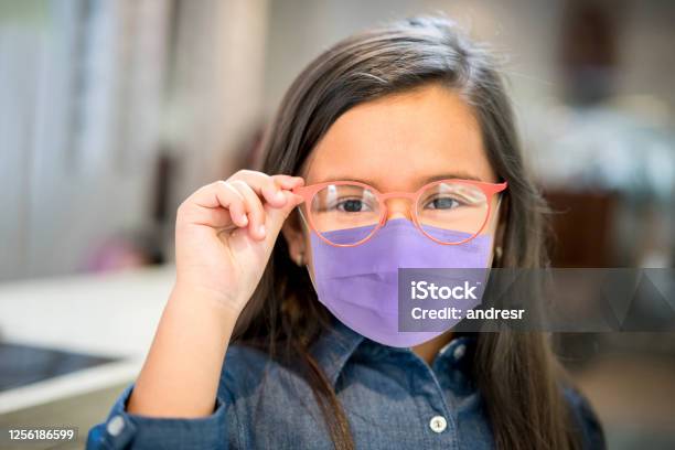 Little Girl Wearing A Facemask While Trying Glasses At The Optician Stock Photo - Download Image Now
