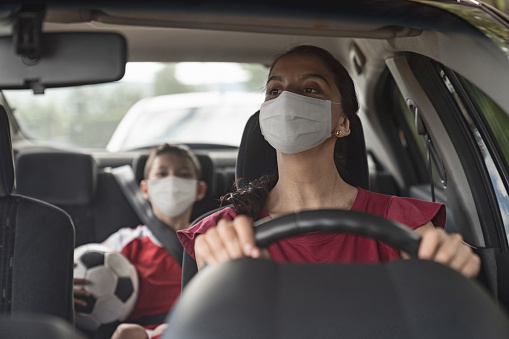 Latin American Mother driving her son to soccer practice wearing a facemask to avoid an infectious disease â COVID-19 lifestyle concepts