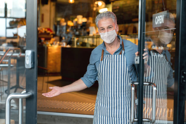 Business owner wearing a facemask and reopening his cafe after the quarantine Business owner wearing a facemask and reopening his cafe after the quarantine - COVID-19 lifestyle concepts opening stock pictures, royalty-free photos & images