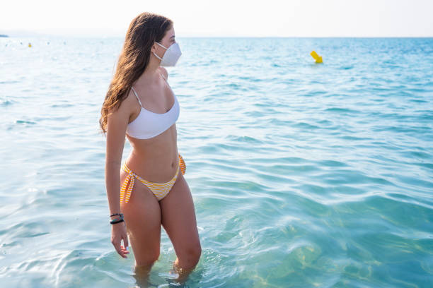 tourist bikini girl with face mask in pandemic on beach - stretch beach imagens e fotografias de stock